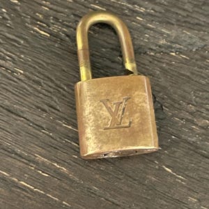 Peut inclure: Un cadenas en laiton vintage avec une anse incurvée. La serrure porte les initiales "LV" en relief sur le devant. Le cadenas est de couleur or vieilli et chaleureux.