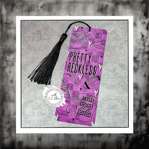 May include: A bookmark with a black tassel and a purple and white design. The bookmark features the text "PRETTY RECKLESS" and various illustrations, including a football, jersey, and key.