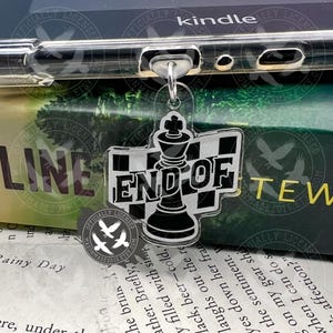 May include: A clear acrylic keychain featuring a black and white chess king design with the words "END OF" on a checkered background. The keychain is attached to a clear phone case, with the word "kindle" visible.