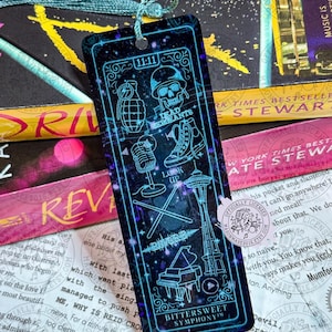 May include: A rectangular bookmark with a dark blue and purple galaxy-themed background featuring light blue line art illustrations of a grenade, skull, microphone, high-top sneaker, Space Needle, drumsticks, and piano with the text 11:11 and Bittersweet Symphony.