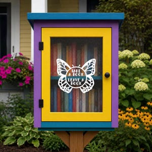May include: A small, rectangular outdoor library box with a bright yellow door frame and purple outer trim. The glass door features a white butterfly decal with the text "TAKE A BOOK LEAVE A BOOK" in the center. Books are visible inside.