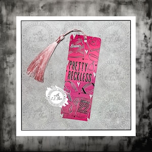 May include: A pink bookmark with a tassel, featuring the text "Pretty Reckless" and illustrations of football gear and a jersey with the number 22. The word "Saints" is also visible.