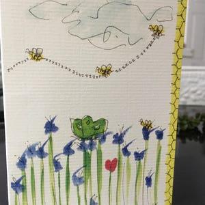 Puede incluir: Una pintura de acuarela de una mariposa verde posada sobre una flor azul con un corazón rojo en el fondo. La pintura también presenta una línea de abejas amarillas volando en fila.