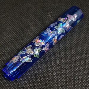 Puede incluir: Bol&iacute;grafo azul con dise&ntilde;o de mariposas iridiscentes. El bol&iacute;grafo es de color azul oscuro con un acabado brillante. Las mariposas parecen flotar sobre la superficie. El bol&iacute;grafo tiene un extremo roscado, mide unos 15 cm.