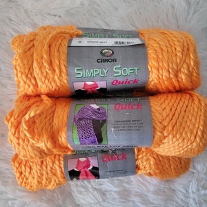 May include: Three skeins of Caron Simply Soft Quick yarn in the color Mango. The yarn is a bright orange color and is made of a soft, bulky acrylic.