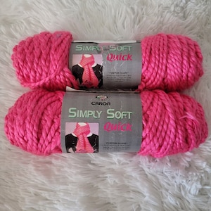 May include: Two skeins of Caron Simply Soft Quick yarn in a bright pink color. The label reads "Simply Soft Quick" and "Pompon Scarf".