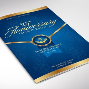 May include: A blue and gold invitation for a 25th anniversary charity ball. The invitation features a gold ribbon, a gold circle with a stylized water drop and hands, and the text "25th Anniversary Charity Ball". The invitation also includes the text "Building Bridges Saving Lives Since 1992" and "The Woodlands Country Club May 23, 2022".