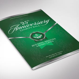 以下が含まれることがあります： 25 周年チャリティボールの緑色のパンフレット。表紙には、白い筆記体で「25th Anniversary Charity Ball」という文字があり、その下に「Building Bridges Saving Lives」という言葉があります。The Woodlands Country Club May 23, 2022.
