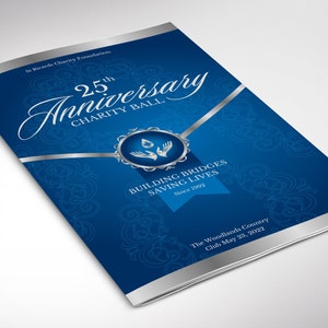May include: A blue and silver programme for a 25th anniversary charity ball. The programme features a silver ribbon, a silver circle with a stylised image of hands holding a drop of water, and the text "Building Bridges Saving Lives Since 1992". The programme also includes the text "The Woodlands Country Club May 28, 2022".