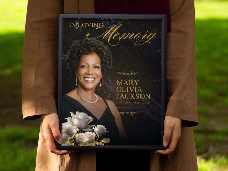 Puede incluir: Una placa conmemorativa enmarcada en negro con una inscripci&oacute;n dorada que dice "In Loving Memory Mary Olivia Jackson" y una foto de una mujer con un ramo de rosas blancas.
