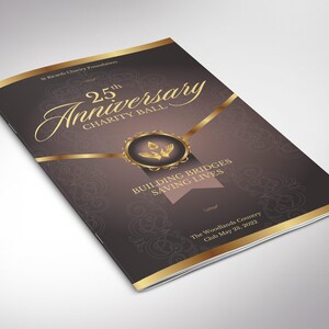 Op de afbeelding: Een brochure voor het 25-jarig jubileum liefdadigheidsbal. De omslag is donkerbruin met gouden accenten en tekst. De tekst bevat "25th Anniversary Charity Ball" en "Building Bridges Saving Lives".