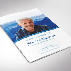 Op de afbeelding: Een gedenkboekje met een portret van een lachende man tegen een blauwe bergachtergrond. De tekst "In Loving Memory of John East Copeland" staat in blauw geschreven, samen met data en kerkgegevens.