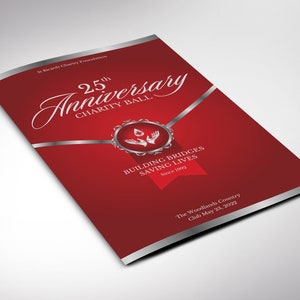 May include: Red and silver invitation for a 25th anniversary charity ball. The invitation features a silver ribbon with a silver seal and the text "Building Bridges Saving Lives Since 1992". The text "25th Anniversary Charity Ball" is in a white cursive font. The Woodlands Country Club May 23, 2022.