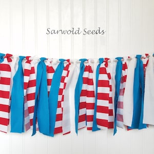 May include: A red, white, and blue fabric banner with a knotted design. The banner is made of strips of fabric with red and white stripes, solid blue fabric, and solid white fabric.
