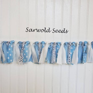 Puede incluir: Una pancarta de tela azul y blanca con lunares blancos y tela de purpurina plateada. La pancarta est&aacute; enhebrada en un fondo blanco y dice "Sarwold Seeds" en la parte superior.