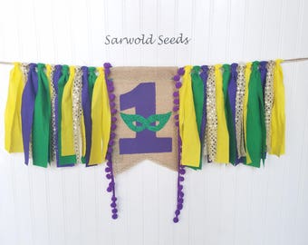 May include: Purple, green, gold, and silver fabric bunting with a burlap banner featuring a purple number one with a green mask. The banner reads "Sarwold Seeds".