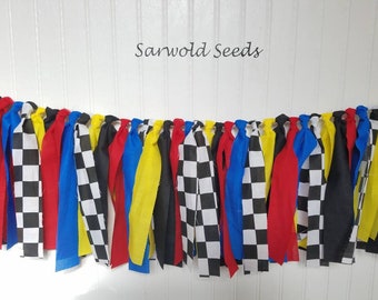 May include: A black, red, yellow, and blue fabric banner with checkered flags. The banner says "Sarwold Seeds" at the top.