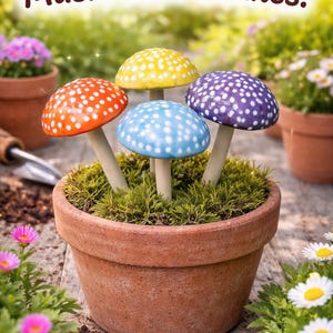 May include: Four ceramic mushroom stakes with rounded caps in orange, yellow, light blue, and purple, each featuring white polka dots and a smooth stem. The text "Whimsical Ceramic Mushroom Stakes!" appears at the top of the image.