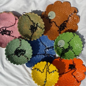 May include: Seven ceramic hanging planters in various colors and patterns, each with a black metal chain. The planters are shaped like scalloped circles and have a textured surface.