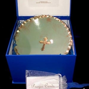 May include: A blue box with a green and gold ceramic dish with a gold cross inside. The dish is in a white organza bag. The box also contains a white card with the words "Prayer Cards" printed on it.