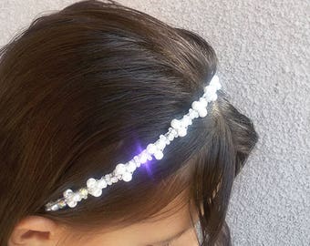 May include: A white pearl and crystal headband with a delicate design. The headband is worn by a person with long brown hair.
