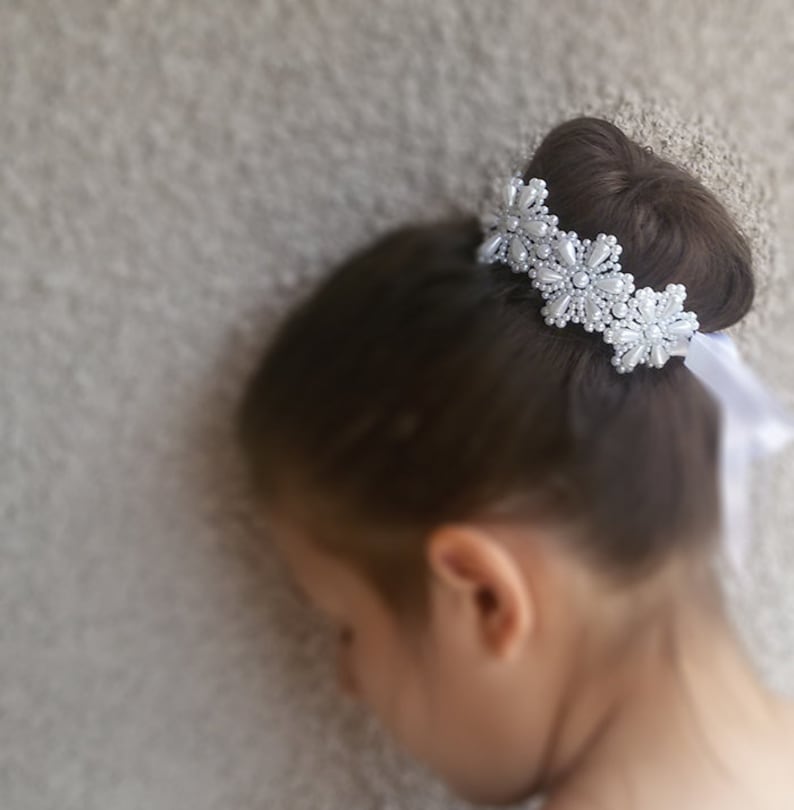 May include: A white pearl hair comb with a floral design. The comb is worn in a bun in a person's hair.