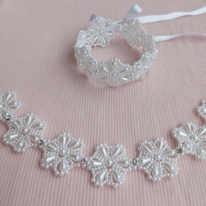 May include: A white pearl necklace and bracelet set with flower-shaped designs. The necklace has five flower motifs and the bracelet has eight.