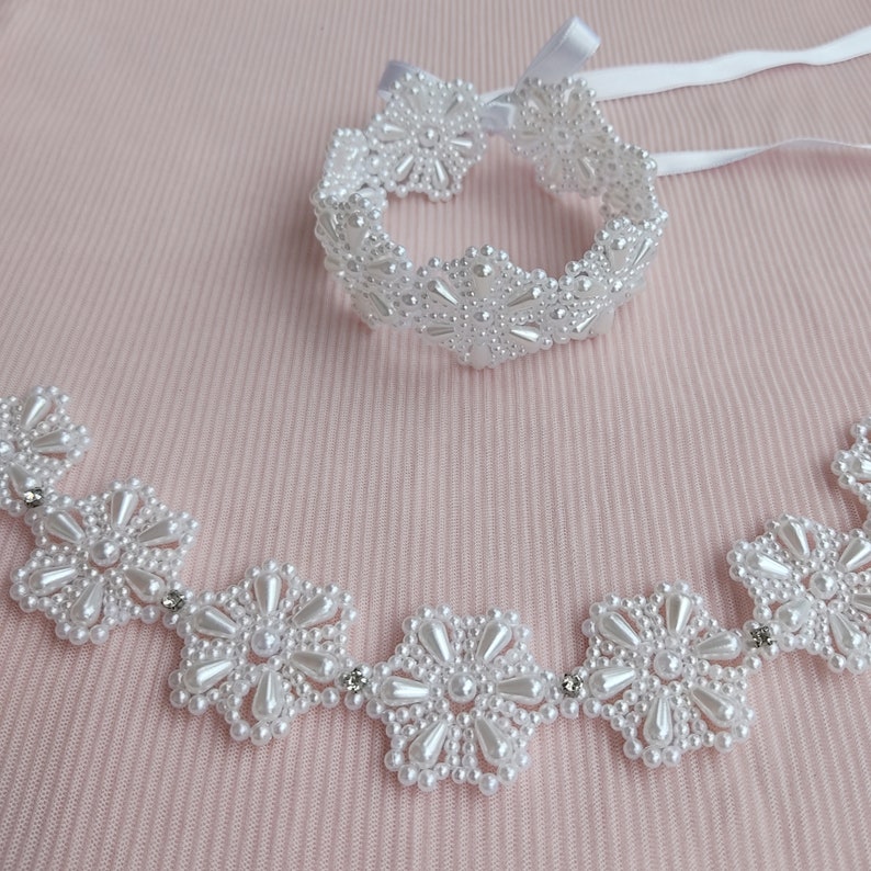May include: A white pearl necklace and bracelet set with flower-shaped designs. The necklace has five flower motifs and the bracelet has eight.