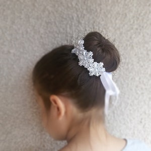 May include: White pearl hair accessory with a white satin ribbon. The accessory is worn in a bun.