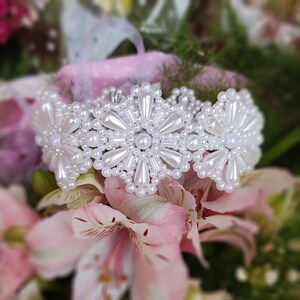 May include: A white pearl bracelet with a flower design. The bracelet is made of small, white pearls that are arranged in a circular pattern to form flowers. The bracelet is delicate and feminine.