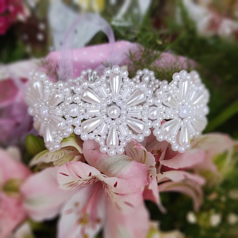 May include: A white pearl bracelet with a flower design. The bracelet is made of small, white pearls that are arranged in a circular pattern to form flowers. The bracelet is delicate and feminine.