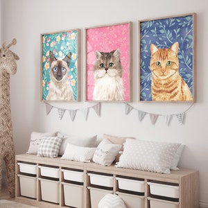 Puede incluir: Tres retratos de gatos enmarcados con fondos florales. Los gatos son un siamés, un persa y un atigrado. Los marcos son de madera clara y los retratos están colgados en una pared blanca.