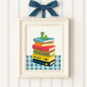 May include: A framed print featuring a stack of colorful books with titles like "The Gruffalo" and "Bugs." A green cartoon caterpillar with glasses sits atop the books. A blue velvet bow adorns the top of the frame. The background has blue and white stripes.