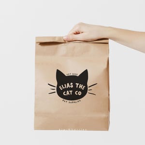 Puede incluir: Una bolsa de papel marr&oacute;n con un logotipo de gato negro que dice "Elias the Cat Co. Pet Supplies" y "Est. 2020". La bolsa tambi&eacute;n tiene el texto "kiwinberries" impreso en la parte inferior.