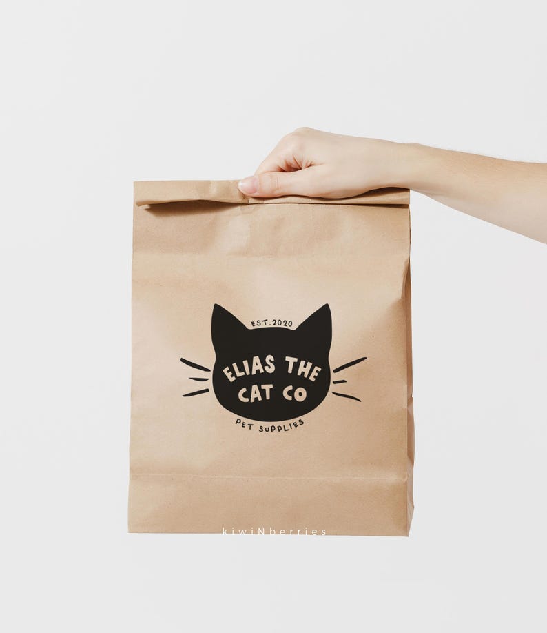 Puede incluir: Una bolsa de papel marr&oacute;n con un logotipo de gato negro que dice "Elias the Cat Co. Pet Supplies" y "Est. 2020". La bolsa tambi&eacute;n tiene el texto "kiwinberries" impreso en la parte inferior.