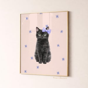 May include: A framed art print featuring a black cat with a blue bow, set against a pink background adorned with blue snowflake designs. The cat has green eyes and a fluffy coat. The frame is gold.