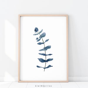 May include: A watercolour painting of a blue eucalyptus branch with leaves. The painting is framed in a light wood frame.
