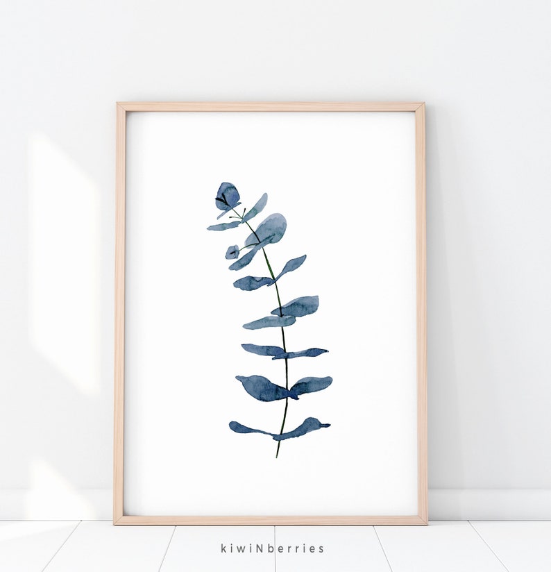 May include: A watercolour painting of a blue eucalyptus branch with leaves. The painting is framed in a light wood frame.