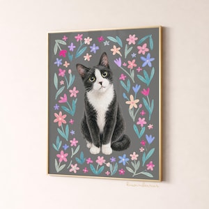 May include: A framed art print featuring a black and white cat surrounded by colorful flowers on a gray background. The cat has green eyes and a curious expression. The artwork is framed in a gold-colored frame.