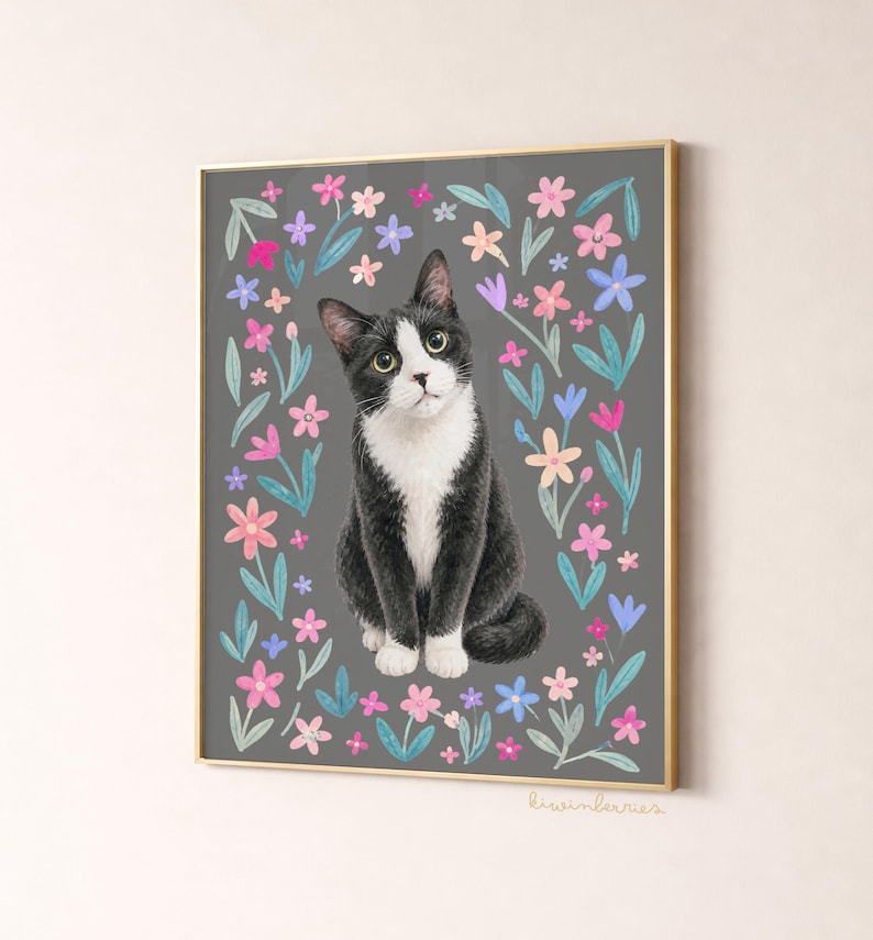 May include: A framed art print featuring a black and white cat surrounded by colorful flowers on a gray background. The cat has green eyes and a curious expression. The artwork is framed in a gold-colored frame.