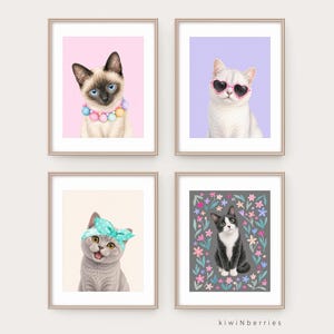 May include: Four framed cat art prints. One print features a Siamese cat with a colorful beaded collar on a pink background. Another shows a white cat wearing heart-shaped sunglasses on a purple background. The other two prints show a gray cat with a blue headband and a black and white cat surrounded by flowers.