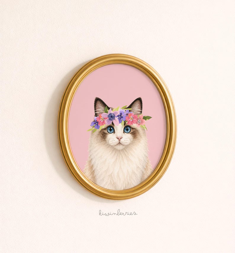 May include: An oval framed print featuring a Ragdoll cat with blue eyes and a floral crown. The cat is set against a pink background, within a gold-colored frame. The artist's signature, "kiwinberries," is at the bottom.