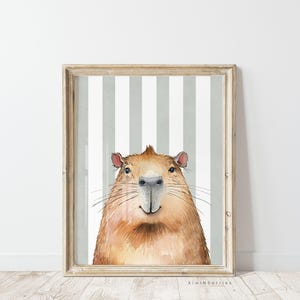 May include: A watercolour illustration of a capybara with a striped background. The capybara is looking directly at the viewer with a friendly expression. The illustration is framed in a light wood frame.
