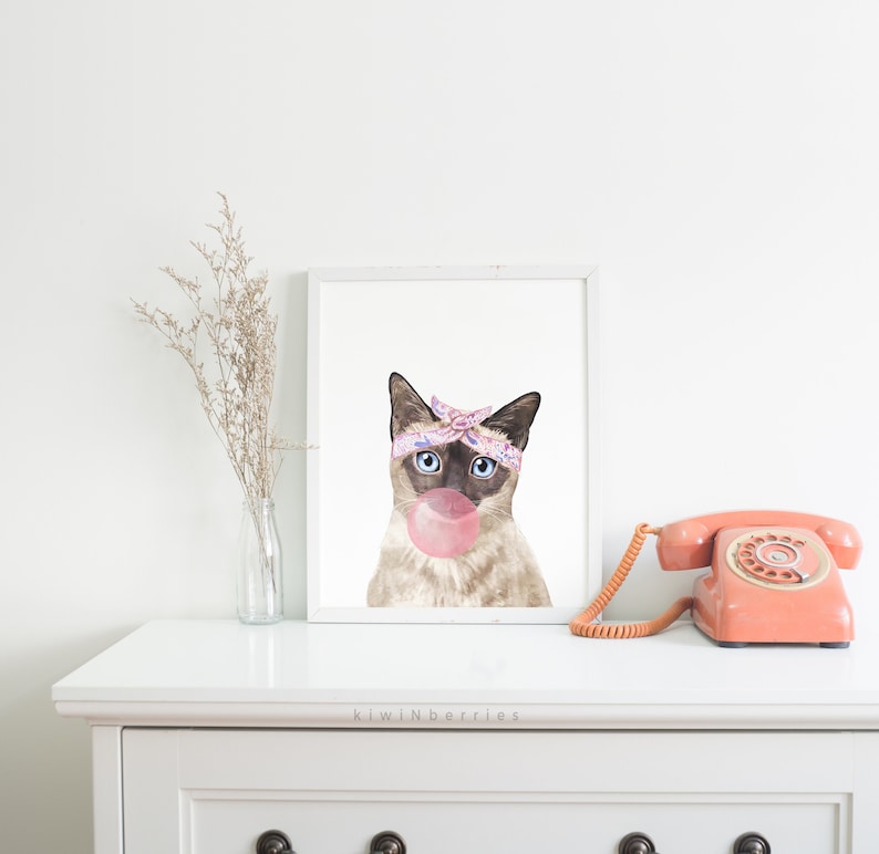 Puede incluir: Una ilustraci&oacute;n de acuarela de un gato siam&eacute;s con un pa&ntilde;uelo rosa y morado y soplando una burbuja rosa. El gato tiene ojos azules y mira directamente al espectador. El fondo es blanco.