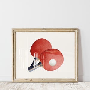 May include: A framed print of a watercolor illustration of two red ping pong paddles and a white ball.