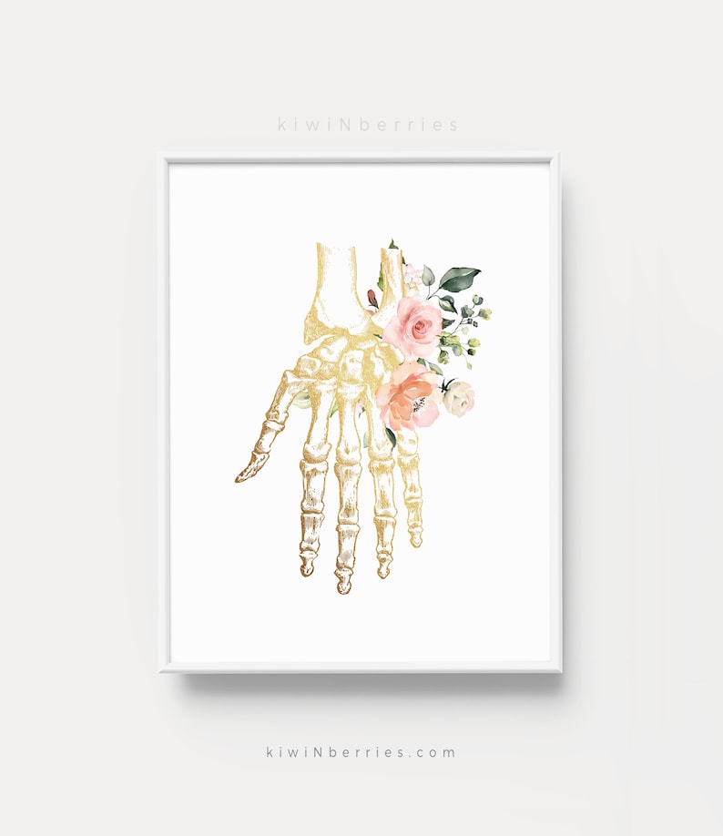 Puede incluir: Un esqueleto de mano anat&oacute;mico dorado con flores de acuarela rosa y melocot&oacute;n. Las flores est&aacute;n dispuestas alrededor de los huesos de la mano y la mu&ntilde;eca. El fondo es blanco.