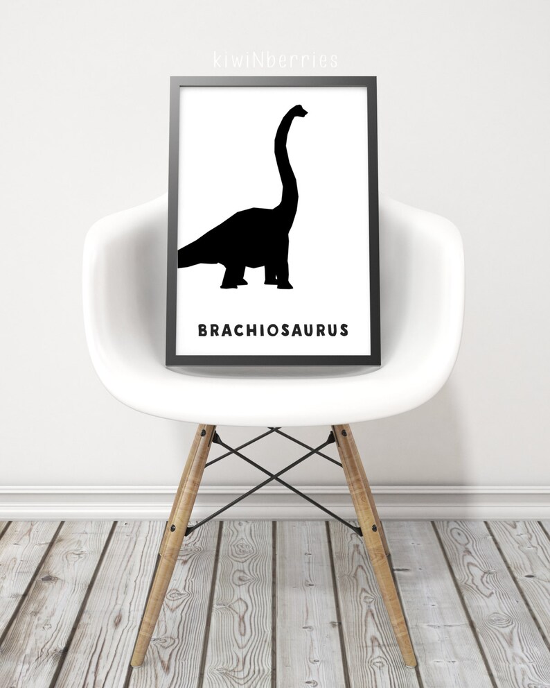 Op de afbeelding: Zwart-witte silhouet van een Brachiosaurus-dinosaurus op een witte achtergrond. De naam van de dinosaurus is in zwarte tekst onder de silhouet gedrukt. De afbeelding is ingelijst en wordt op een witte stoel getoond.