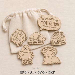 Op de afbeelding: Een beige katoenen buidel met trekkoord en vijf lichtgekleurde houten uitsparingen met gegraveerde illustraties en tekst. De ontwerpen bevatten een vlam, een blobvis, een pissebed, een vogel en een slak, met zinnen zoals A POCKETFUL OF MOTIVATION.