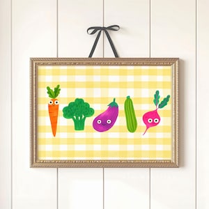 May include: A framed print featuring whimsical illustrations of vegetables: a carrot, broccoli, eggplant, zucchini, and beet. The artwork has a yellow and white checkered background and is framed in a gold-colored frame. The print is suspended by a black ribbon.