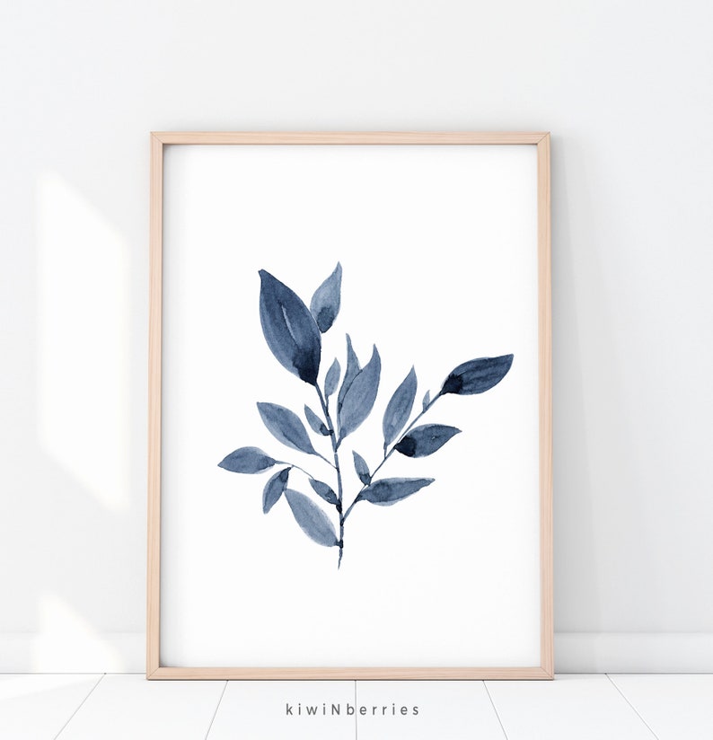 May include: A watercolour painting of a blue leafy branch with a white background. The painting is framed in a light wood frame.